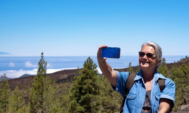 海の上のテネリフェ島の地平線の山の風景を旅する自撮りをしている幸せな年配の女性、アクティブな引退した高齢者と楽しいコンセプト