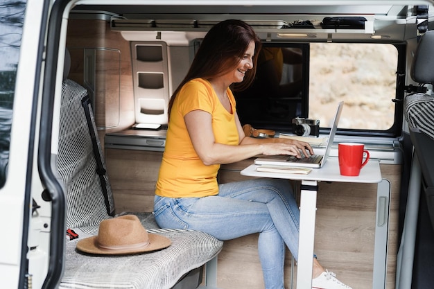 Photo happy senior woman using computer laptop inside camper mini van  focus on face