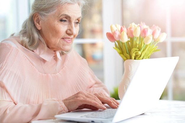 Счастливая старшая женщина используя компьтер-книжку