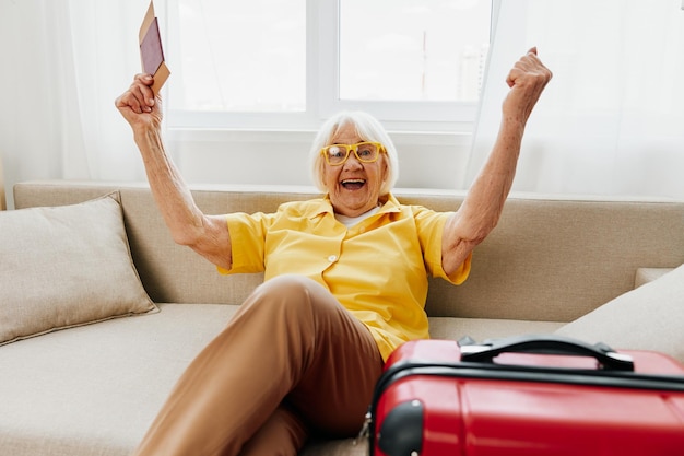 Happy senior woman with passport and travel ticket packed a red suitcase vacation and health care Smiling old woman happily sits on the sofa before the trip