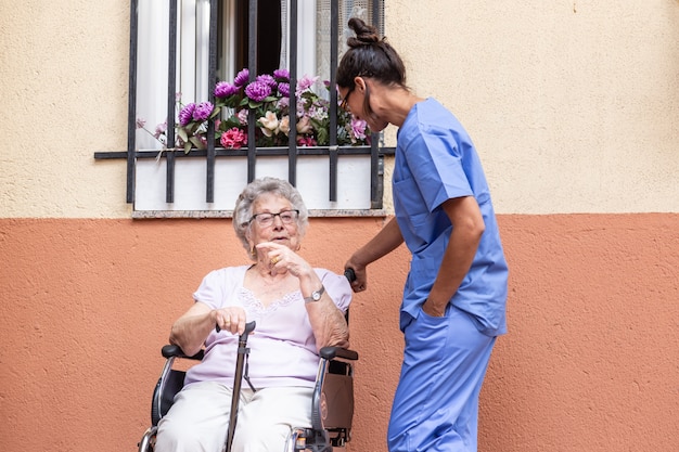 Happy senior woman with walking stick in wheelchair with her caregiver at home