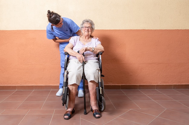 自宅で彼女の介護者と車椅子の杖を持つ幸せな年配の女性