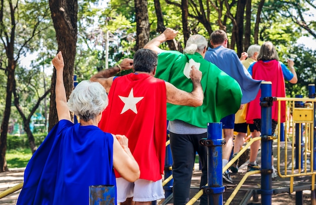 Happy seniors wearing superhero costumes at a playground