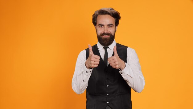 Happy server gives like symbol on camera, expressing his approval with okay gesture. professional restaurant employee giving thumbs up to show positive sign, working in catering industry