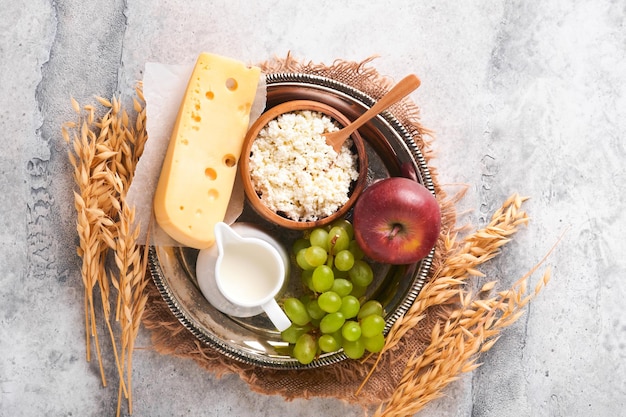シャブオットのお祝いのための幸せなシャブオットの背景牛乳とチーズ熟した小麦と果物青い木製の背景古い灰色のテーブルの上の乳製品コンクリートの背景シャブオットのコンセプトモックアップ