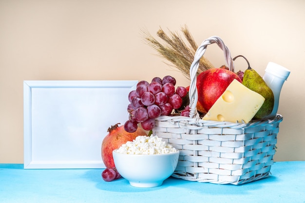 Happy Shavuot greeting card background with food Symbols of jewish Shavuot holiday pomegranate grapes apple sweet challah bread wheat spikelets milk cheese cottage cheese on light blue background