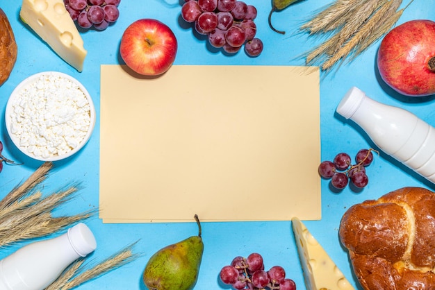 食べ物と幸せなシャブオットのグリーティングカードユダヤ人のシャブオットの休日のシンボルブドウリンゴ甘いシャブオットパン小麦スパイクレットミルクチーズカッテージチーズ水色の背景に