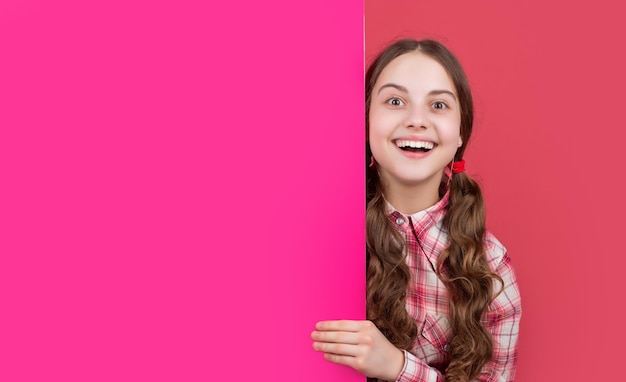광고 복사 공간이 있는 빈 분홍색 종이 뒤에 행복한 충격을 받은 소녀