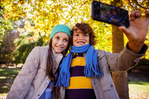 Happy siblings taking selfie at park during autumn