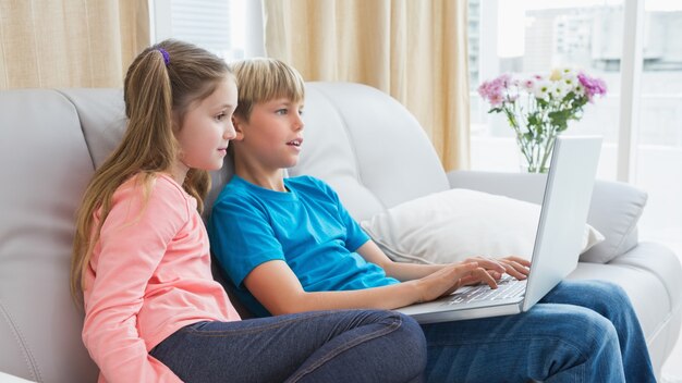 Happy siblings using laptop on sofa