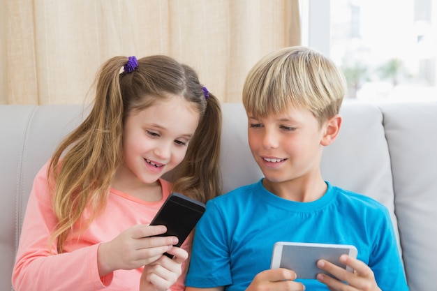 Photo happy siblings using smartphones on sofa