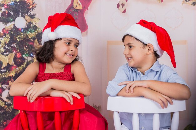 Happy siblings wearing santa hat sitting on chairs at home