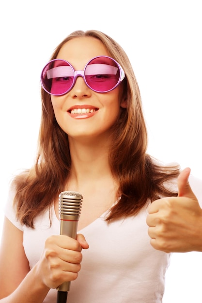 Happy singing girl Beauty woman wearing white tshirt and big sunglasses with microphone over white background ipster styl