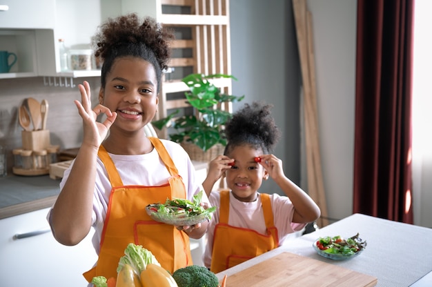 Happy sister black skin with salad on plate in kitchen