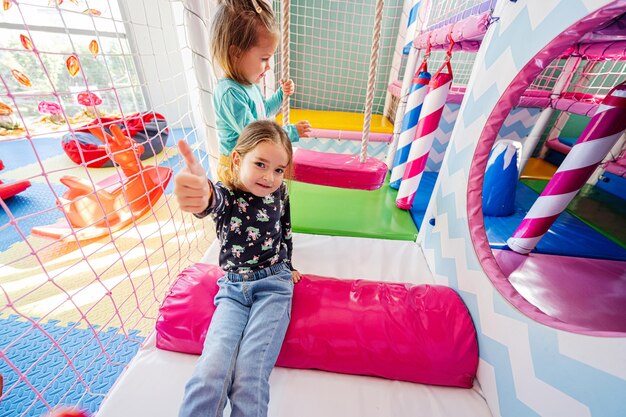 Happy sisters playing at indoor play center playground girl in\
swing