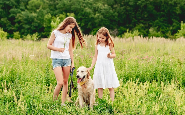 Happy sisters with cute dog on flowering summer meadow