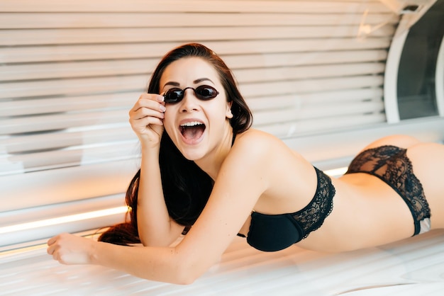 Happy slender brunette girl in swimsuit lies in horizontal sunbed and sunbathes in goggles