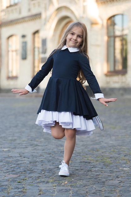 Фото Счастливая маленькая балерина в школьной форме балансирует на ноге балерины на открытом воздухе