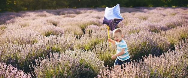 Piccolo ragazzo felice che attraversa un campo di lavanda con un palloncino a stella