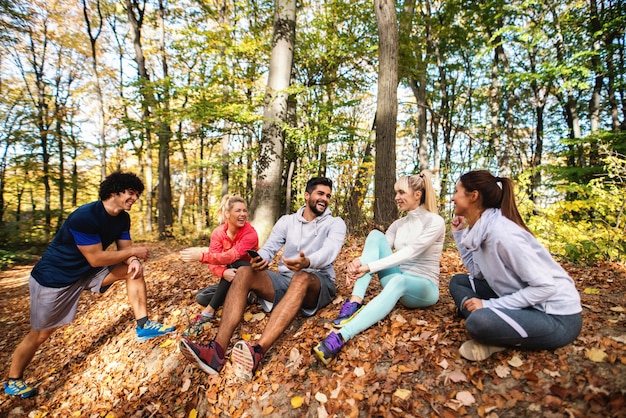 写真 森の中で地面に座ってランニングから休んでいる友人の幸せな小さなグループ。秋の時間。