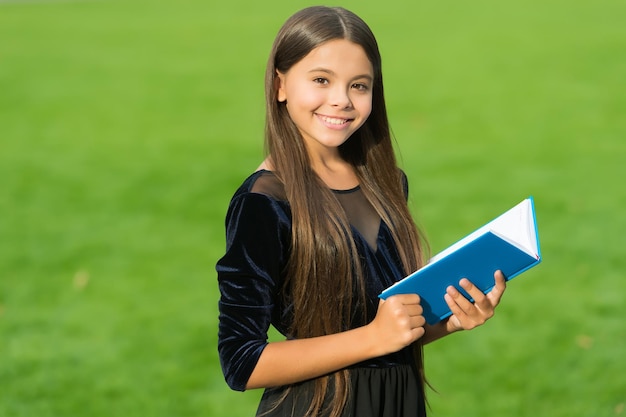 学生服の笑顔で幸せな小さな子供が勉強の本を持って緑の草晴れた夏の屋外教育