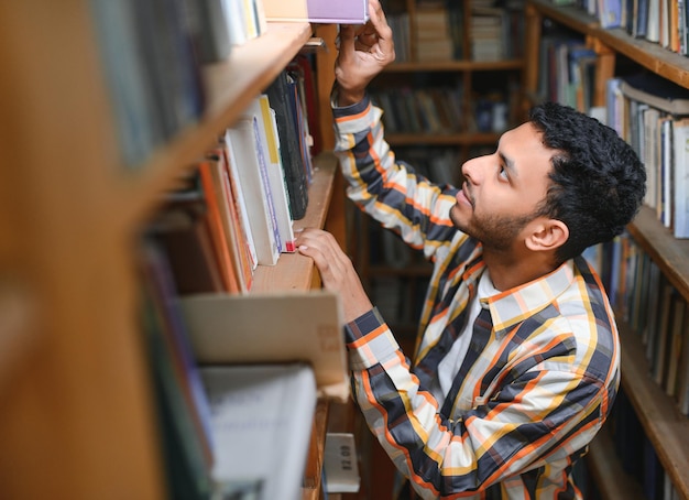 Счастливый умный индийский или арабский парень смешанной расы студент университета в библиотеке