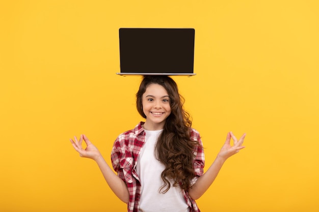 счастливая умная девочка-подросток медитирует с ноутбуком на голове, представляя школьный онлайн-урок, учебу.