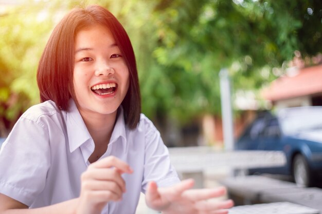 幸せな笑顔アジアの学生の女の子十代の若いかわいい座っている屋外探しのカメラとコピースペース