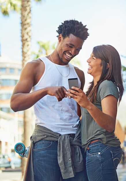 Happy smile and couple on a phone in city watching a comic comedy or funny video on social media Happiness love and interracial man and woman scrolling online on the internet in urban town road