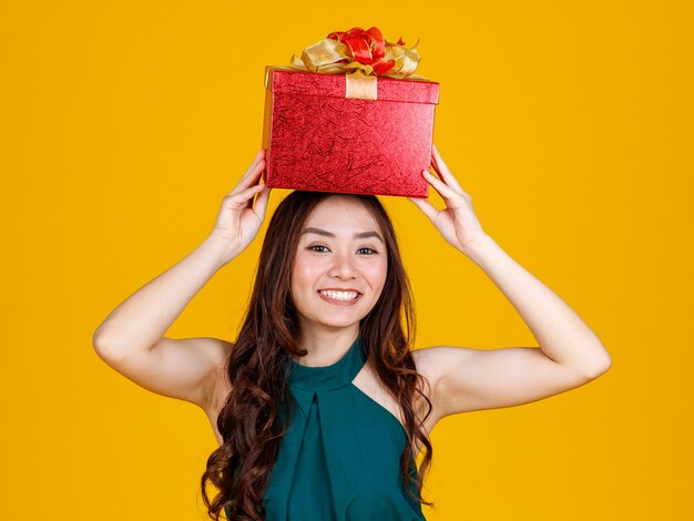 Happy smile face cute asian girl with dark hair holding gift box over head with delightful and excited, studio shot on yellow background. celebrate and festival concept