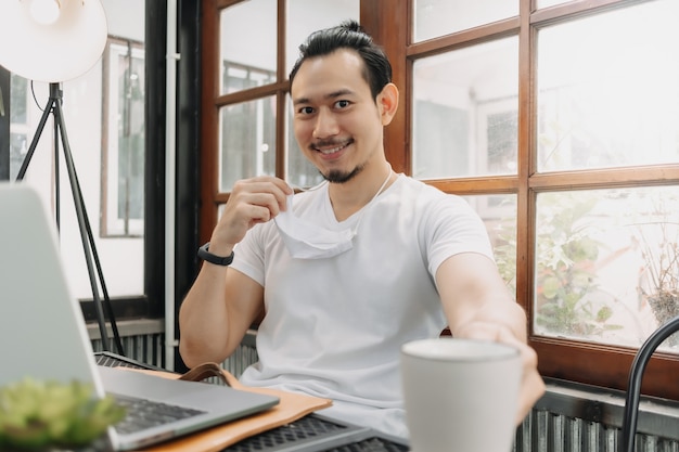 La faccia felice e sorridente dell'uomo beve caffè mentre lavora e indossa la maschera