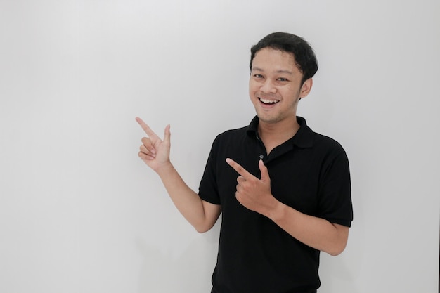 Happy and smile of young Asian man with hand point on empty space Indonesia Man wear black shirt Isolated grey background