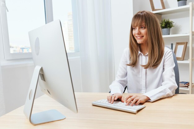 Happy smiling adorable blonde businesswoman worker freelancer look at screen typing answer for clients in light modern office Cheerful employee work on computer online in support service Copy space