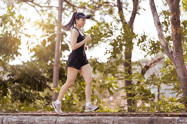 Happy smiling adult Asian woman jogging outdoor in the city park in sunshine beautiful summer day.  Happy relaxed mature woman jogging to live an active and healthy lifestyle