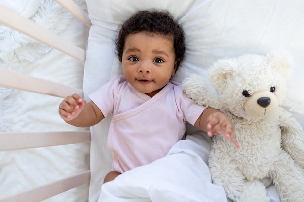 写真 テディベアとベビーベッドで幸せな笑顔のアフリカ系アメリカ人の赤ちゃんが眠りに落ちるか、寝る