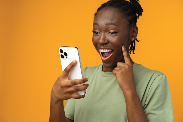 Ragazza afroamericana sorridente felice che utilizza il suo smartphone in studio giallo