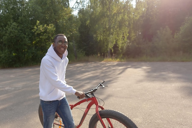 A happy smiling African American man with a bicycle in a public park Sports and recreation