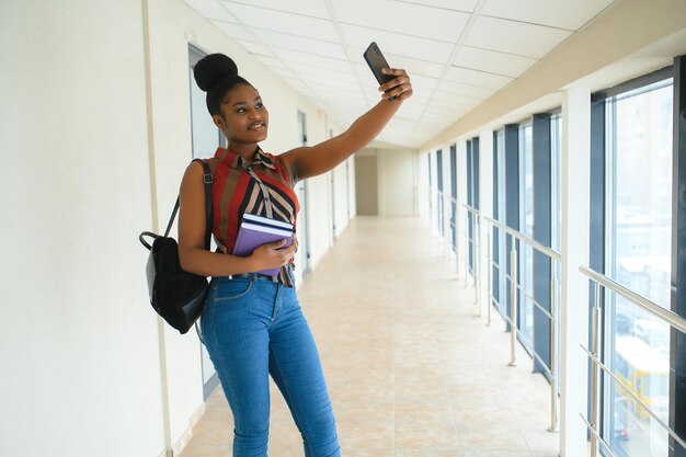 Happy smiling african-american student girl with backpack at\
university background. technology, education, leisure concept