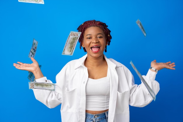 Happy smiling afro american woman throwing money against blue background