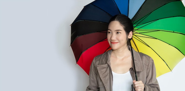 La bella donna asiatica sorridente felice è sotto l'ombrello colorato dell'arcobaleno e distoglie lo sguardo con un sorriso positivo