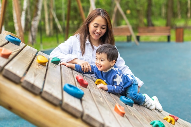 Happy smiling asian mother and child are playing in playground in summer park. Copy space for text