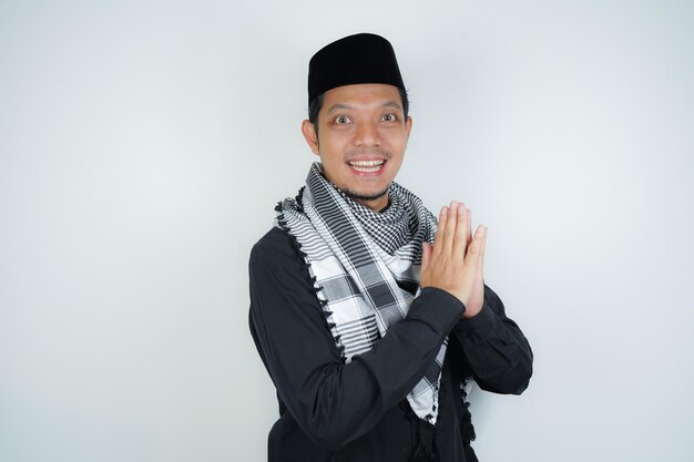 Happy smiling Asian Muslim man in Arabic turban sorban standing with Eid greeting gesture and