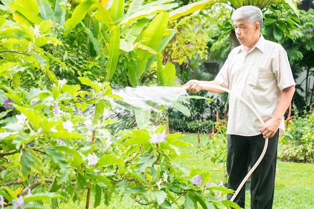 행복하고 웃는 아시아 노인은 집에서 은퇴한 후 취미로 식물과 꽃에 물을 주고 있습니다. 노인을 위한 행복한 생활 방식과 건강의 개념.