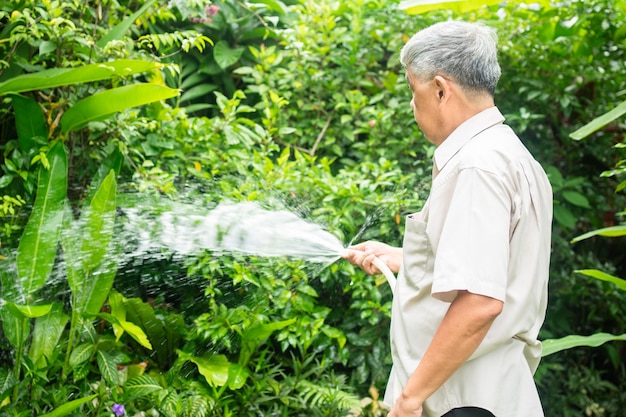 幸せで笑顔のアジアの老人は、退職後の趣味のために植物や花に水をまきます