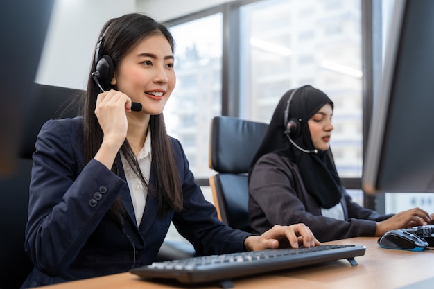 Photo happy smiling asian woman call center and operator wearing headsets working on computer and talking with customer with her service mind
