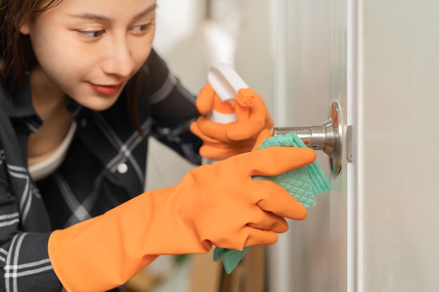 幸せな笑顔のアジアの若い女性の女の子の掃除は、自宅のトイレの部屋のノブのドアにほこりの使用ぼろきれスプレーボトルをこすります家庭衛生掃除クリーナー人々の機器や掃除のためのツール