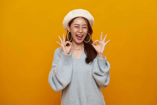 Photo happy smiling asian young woman smiling and showing hand ok sign isolated on yellow background