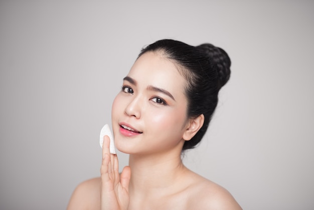 Happy smiling beautiful asian woman using cotton pad cleaning skin.