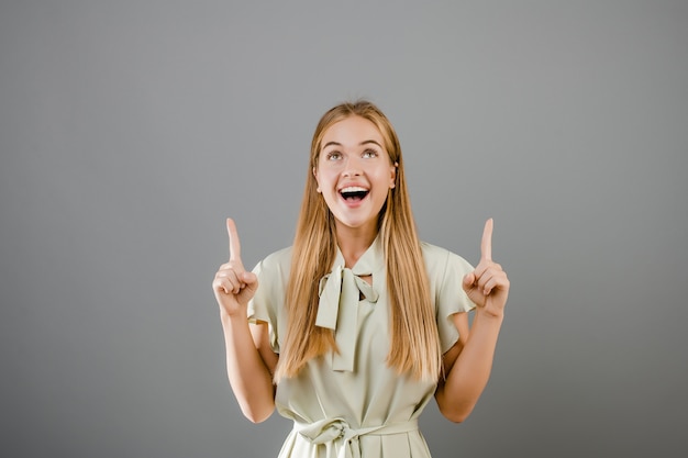 Happy smiling beautiful blonde young woman pointing finger at copyspace isolated over grey