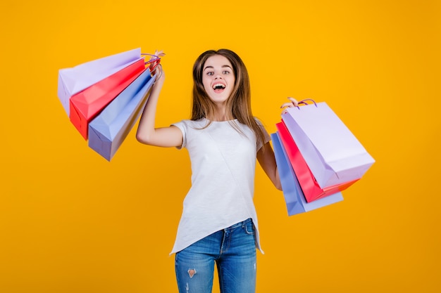 Happy smiling beautiful brunette woman with colorful paper shopping bags jumping in the air  isolated over yellow